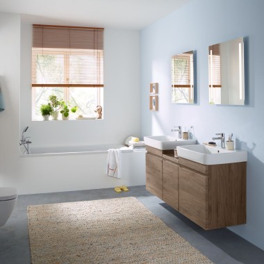 Gezinsbadkamer met lichtblauwe wand en badkamermeubels in noten hickory, spiegelkast, bedieningsplaat, wastafels van Geberit