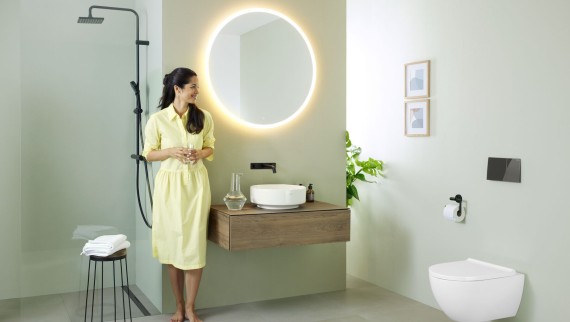 Vrouw in gele jurk voor mintgroene badkamer met meubel, wastafel. spiegel en wc van Geberit en zwarte kranen