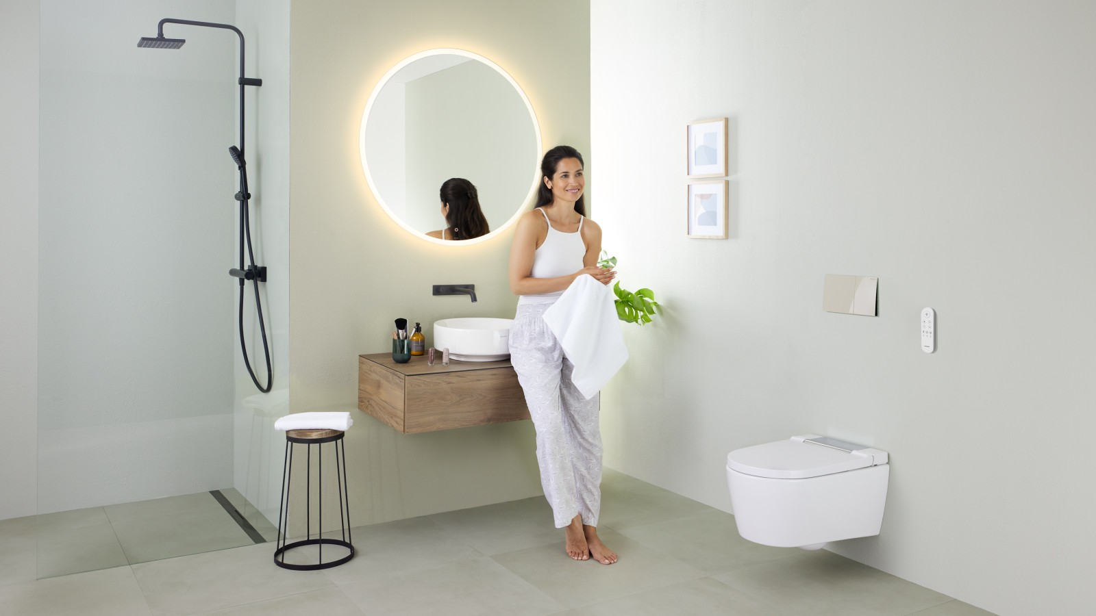 Vrouw leunt op een wastafel in een badkamer met Geberit AquaClean Sela douchewc en Geberit VariForm-wastafel en meubel Vrouw leunt op een wastafel in een badkamer met Geberit AquaClean Sela douchewc en Geberit VariForm-wastafel en meubel