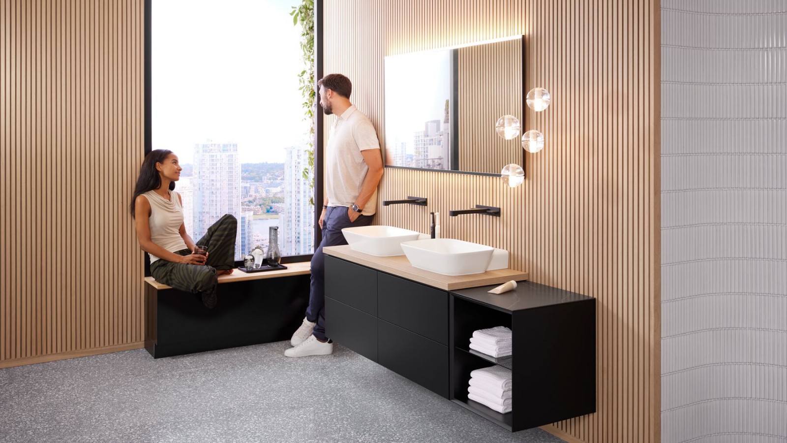 Een vrouw zit op de vensterbank in de badkamer met Geberit ONE producten en praat met een man. Een vrouw zit op de vensterbank in de badkamer met Geberit ONE producten en praat met een man.