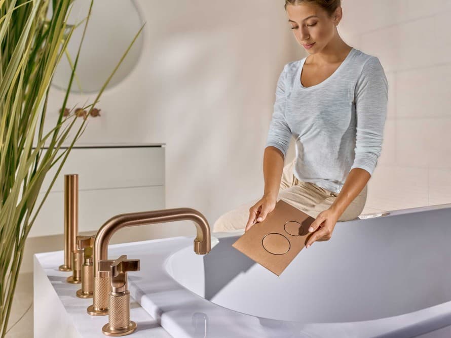 Vrouw in de badkamer met Sigma40 bedieningsplaat in de kleur geborsteld roodgoud, afgestemd op de kleur van de kranen. Vrouw in de badkamer met Sigma40 bedieningsplaat in de kleur geborsteld roodgoud, afgestemd op de kleur van de kranen.